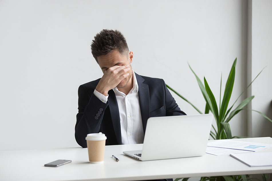 businessman rubbing eyes in front of laptop