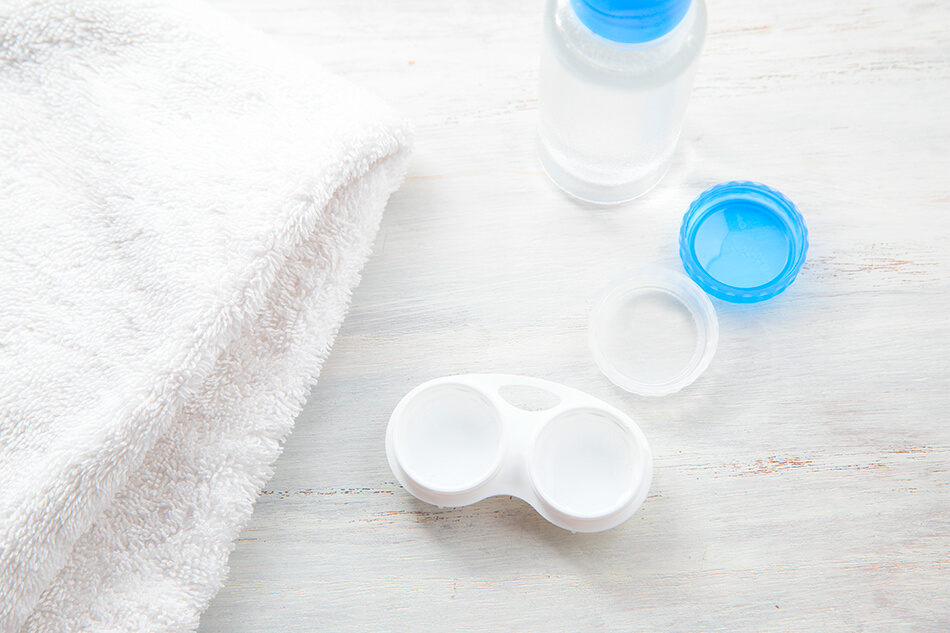 white towel, contact lens case and solution on countertop