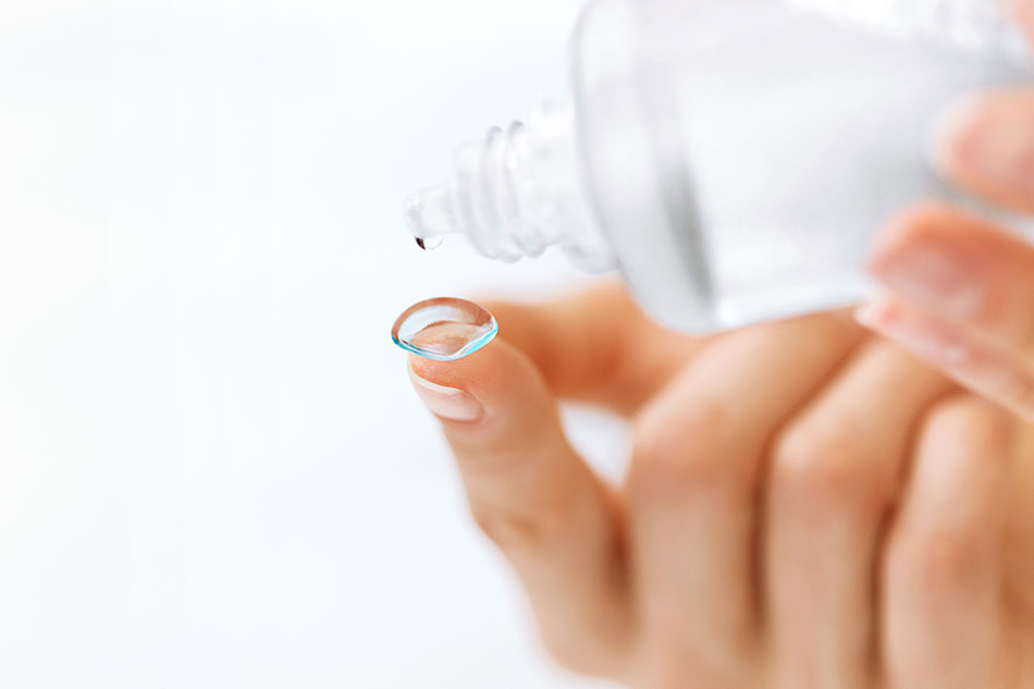 contact lens on fingertip and cleaning solution