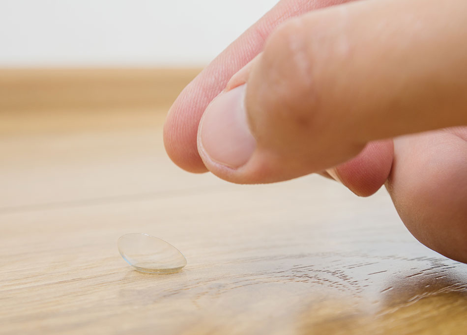 close up of person’s thumb and finger picking up a contact lens on the floor