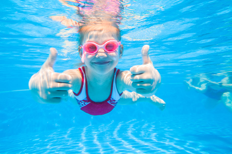 Little girl wearing goggles underwater giving thumbs up