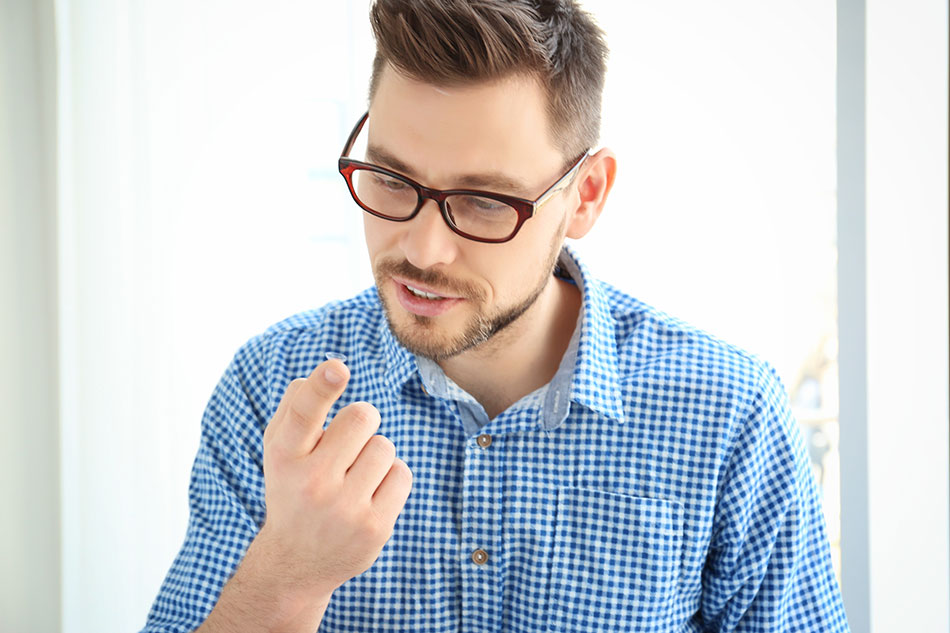 Man with glasses looking at contact lens on finger