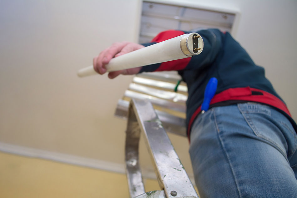 Man on ladder removing light from a fixture in the ceiling