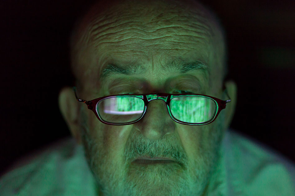 older man looking at screen reflected in eyeglasses