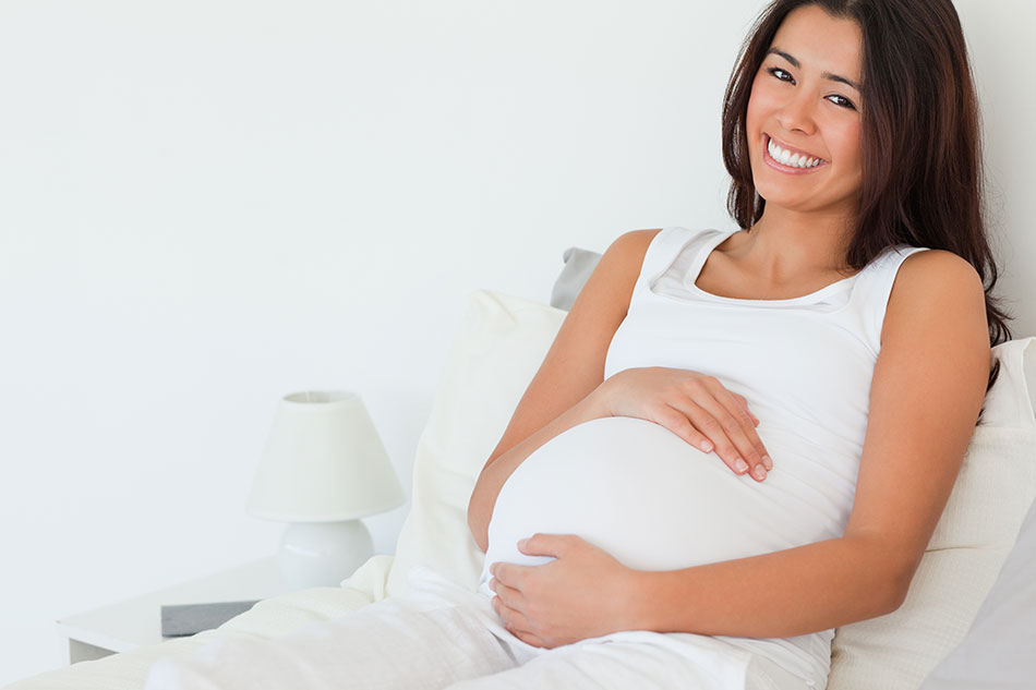 Pregnant woman sitting on bed smiling