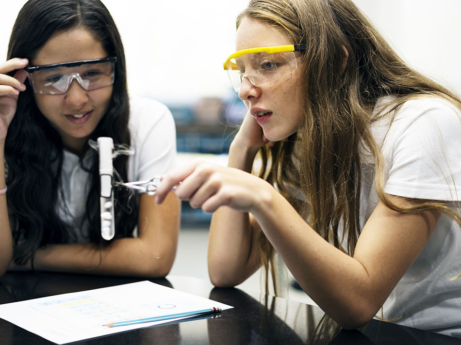 Two schoolgirls doing science experiment with eye protection