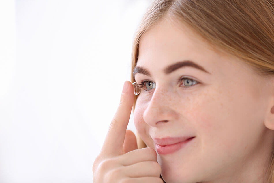 Smiling teen girl putting contact lens in her eye