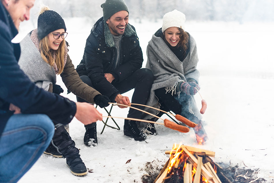 people roasting hotdogs on a campfire in the snow