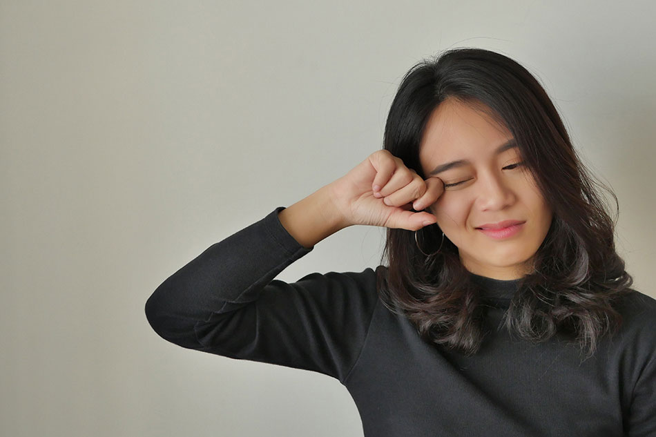 woman in black shirt rubbing her eye