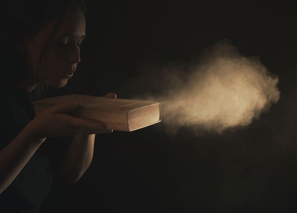 Woman blowing dust off a book
