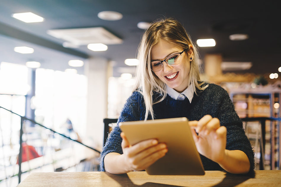 woman in blue sweater and glasses reading on a tablet