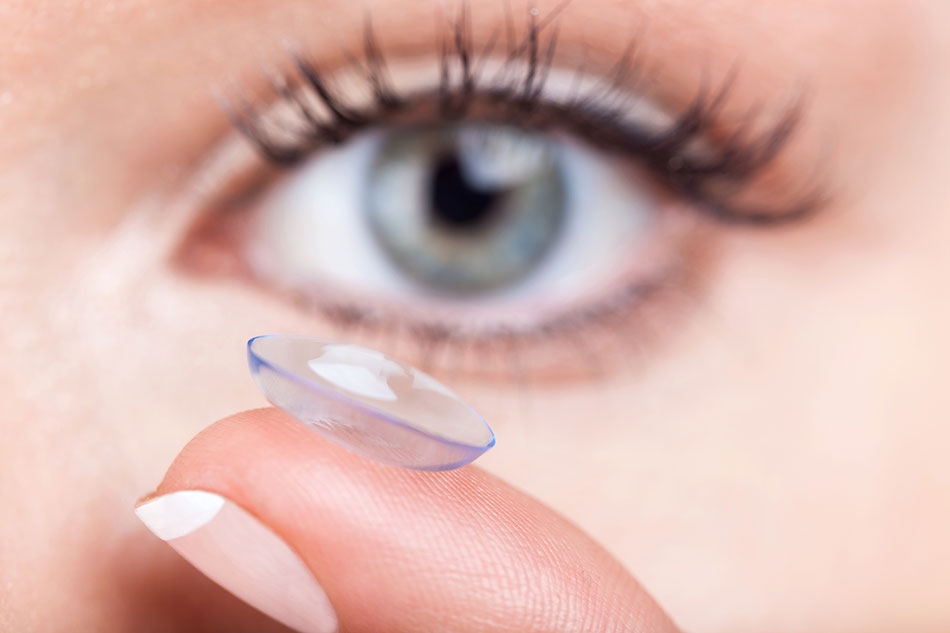 Woman holding holding up a contact lens on her finger