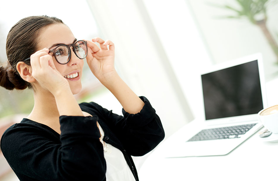 woman wearing glasses and computer in the background