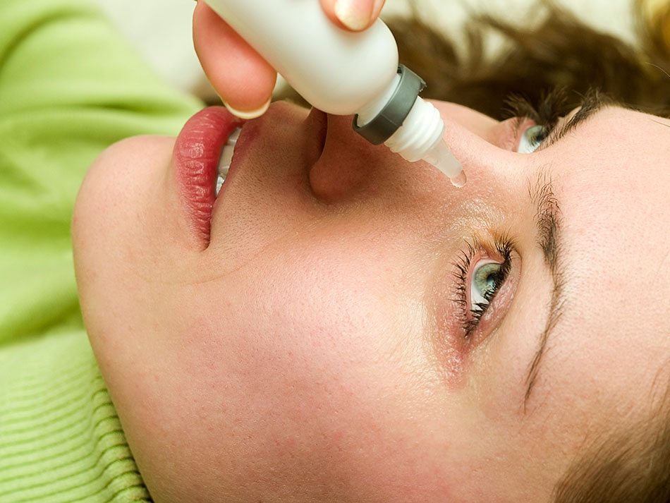 woman lying down applying eye drops with eye drops bottle