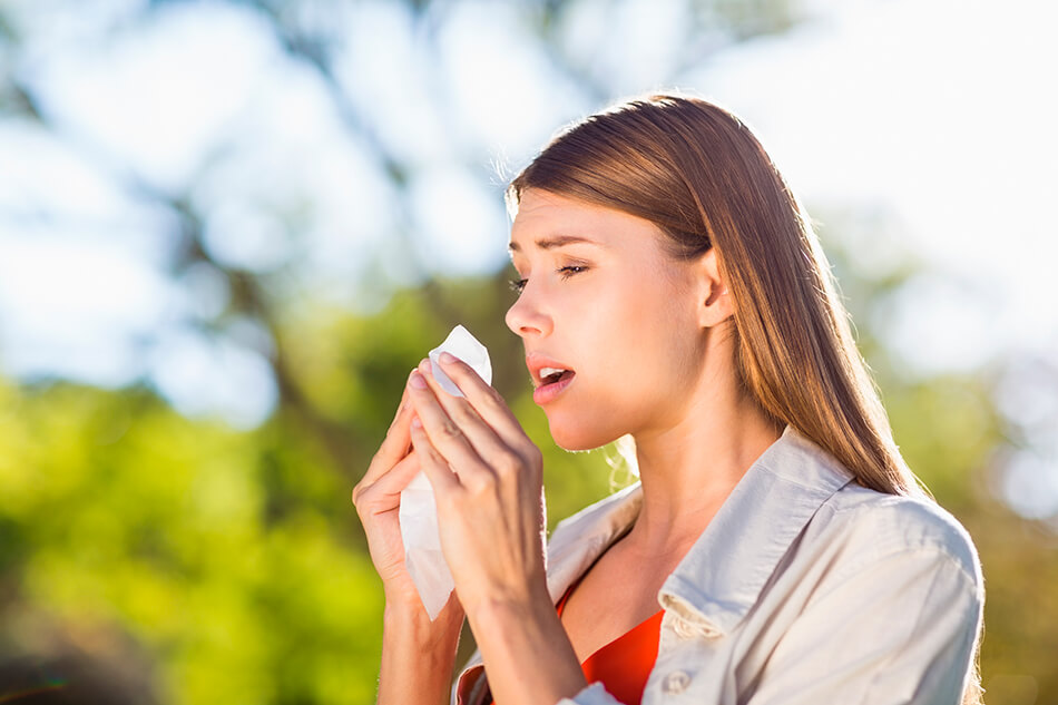 woman sneezing into tissue outdoors