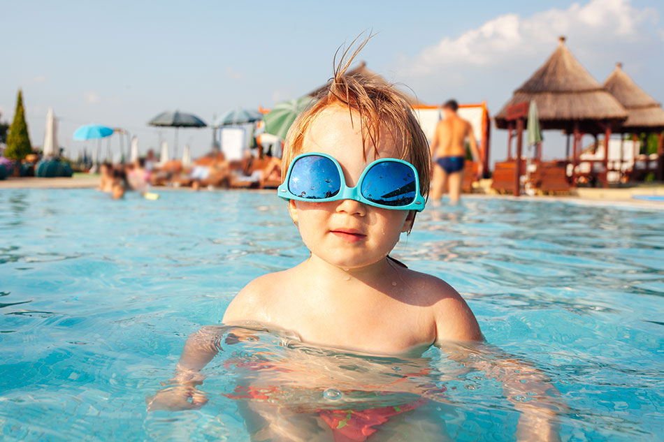 Young child in swimming pool with blue sunglasses on vacation