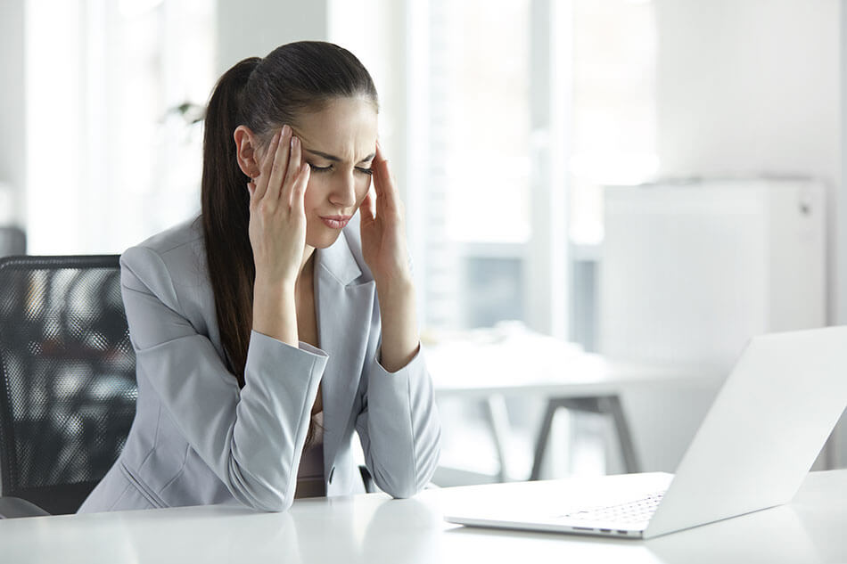 stressed young woman at desk rubbing her temples